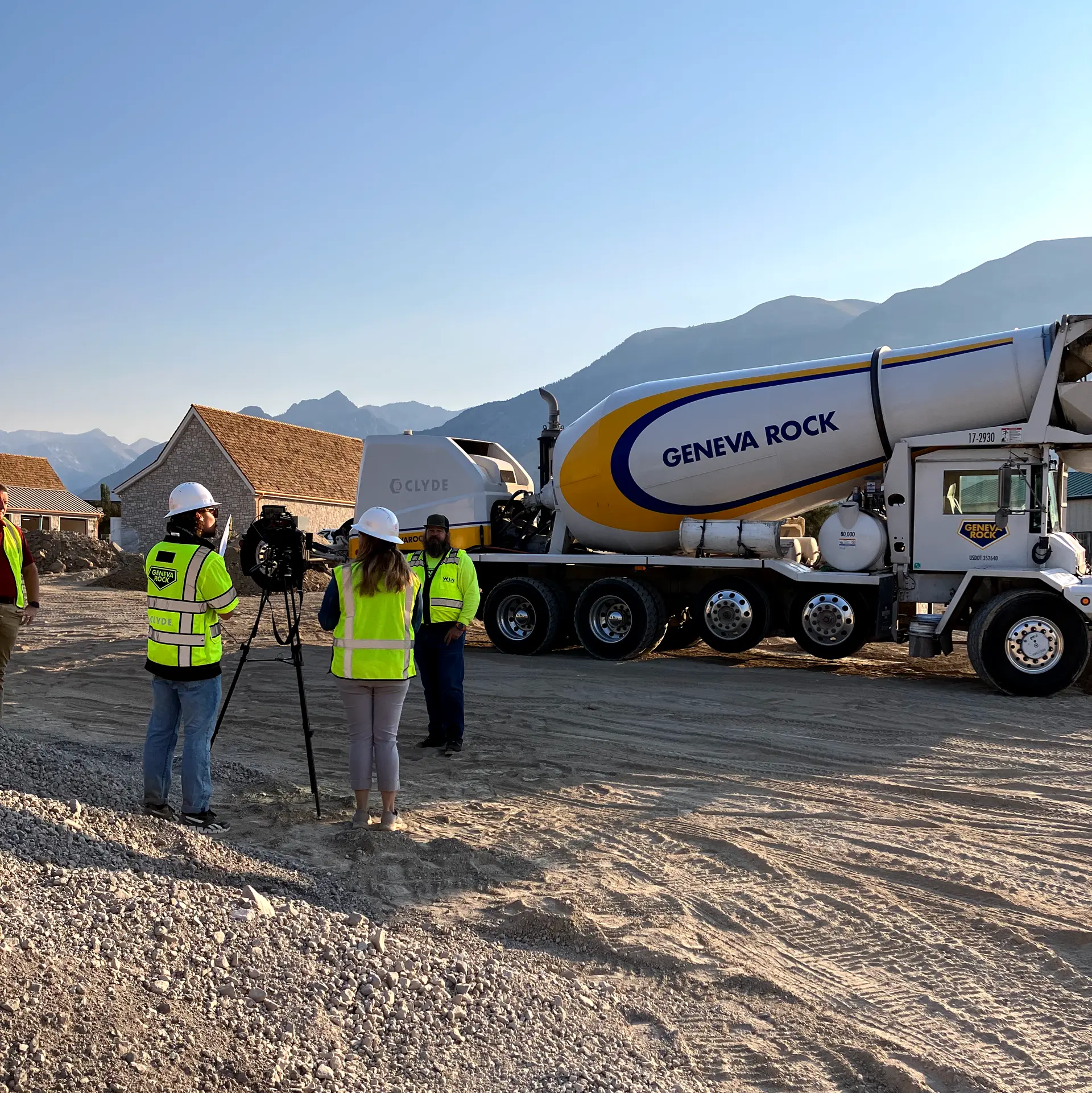 A film crew in hard hats and hi-vis vests interviewing a worker beside a concrete mixer truck on a job site